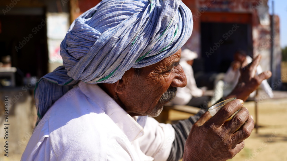 Older man wearing turban and taking a sip of coffee or tea close up face.