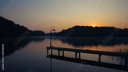 Sunrise on lake with reflections in the water and pier trees and light pole