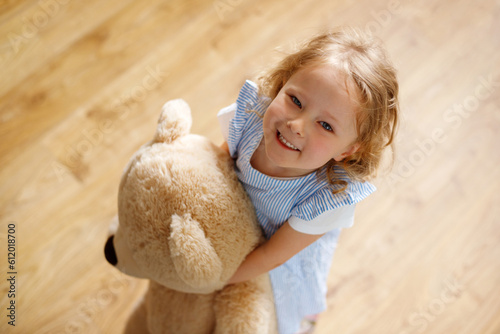 Top-view portrait of adorable girl, about 4 years old, who is looking up and smiling on the blurred background, shows enjoyment and cheerfulness.