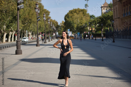 Young and beautiful woman with straight brown hair, wearing an elegant black dress, walking downtown, empowered and independent, smiling and happy. Concept fashion, beauty, empowerment, millennial. © Manuel
