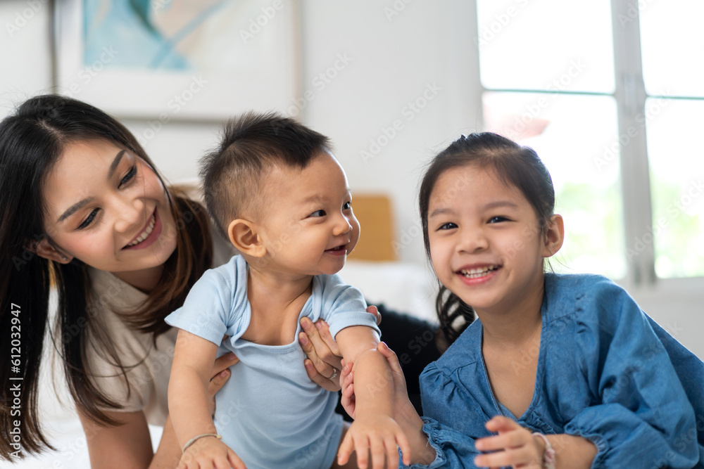 Portrait of enjoy happy love family asian mother playing with adorable little asian baby and sister girl, newborn, infant.Mom touching care with cute son in a white bedroom.Love of family concept Portrait of enjoy happy love family asian mother playing with adorable little asian baby and sister girl, newborn, infant.Mom touching care with cute son in a white bedroom.Love of family concept