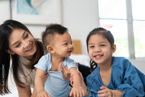 Portrait of enjoy happy love family asian mother playing with adorable little asian baby and sister girl  newborn  infant.Mom touching care with cute son in a white bedroom.Love of family concept