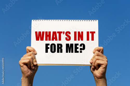 What's in it for me text on notebook paper held by 2 hands with isolated blue sky background. This message can be used as business concept about what's in it for me.