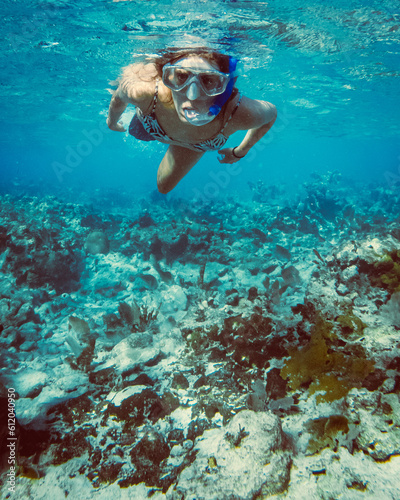 A woman snorkeling over coral in blue waters