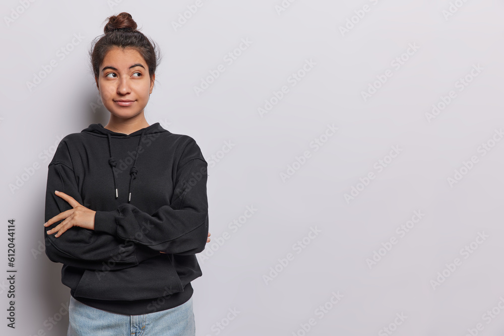 Studio shot of lovely dark haired woman keeps arms folded concentrated aside thoughtfully tries to find solution in mind dressed in casual black sweatshirt and jeans isolated over white background. Studio shot of lovely dark haired woman keeps arms folded concentrated aside thoughtfully tries to find solution in mind dressed in casual black sweatshirt and jeans isolated over white background.