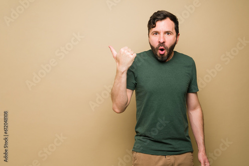 Surprised latin man pointing to copy space with casual clothes