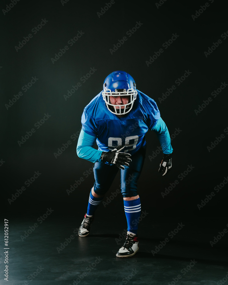 Portrait of a man in a blue uniform for american football runs with a ball on a black background. 
