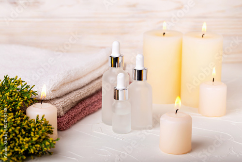 White glass dropper bottles with gel or lotion  oil or toner among burning candles. Towels and plant complete concept of spa treatments. Care and rest  beauty and health. Selective focus
