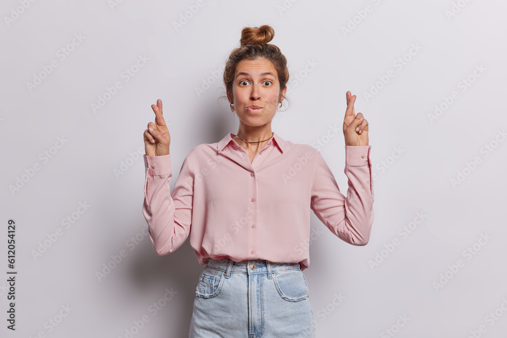 Lovely young European woman stands with anticipation her finger crossed and hopeful smile on face exudes sense of belief in positive outcomes has desire for good fortune dressed in elegant clothes Lovely young European woman stands with anticipation her finger crossed and hopeful smile on face exudes sense of belief in positive outcomes has desire for good fortune dressed in elegant clothes