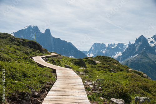 A winding wooden walking path high in the mountains. A panoramic view of the peaks of the Mont Blanc massif