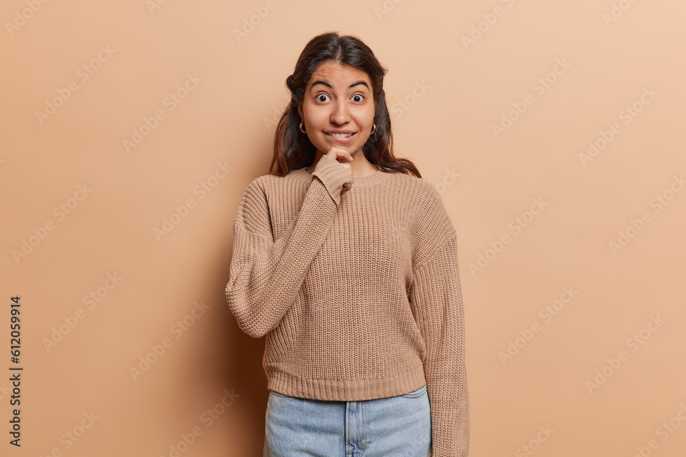 Iranian woman dressed in knitted jumper gazes with expression of wonderment bites lips feels surprised. Her surprise is evident as captures attention of viewers embodying essence of human reactions Iranian woman dressed in knitted jumper gazes with expression of wonderment bites lips feels surprised. Her surprise is evident as captures attention of viewers embodying essence of human reactions