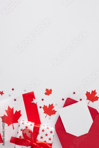 Concept of Victoria Day event. Top view vertical flat lay of red envelope, postcard, gift box in national colors, canadian flag, maple leaves, sparkles on white background with space for text or ad