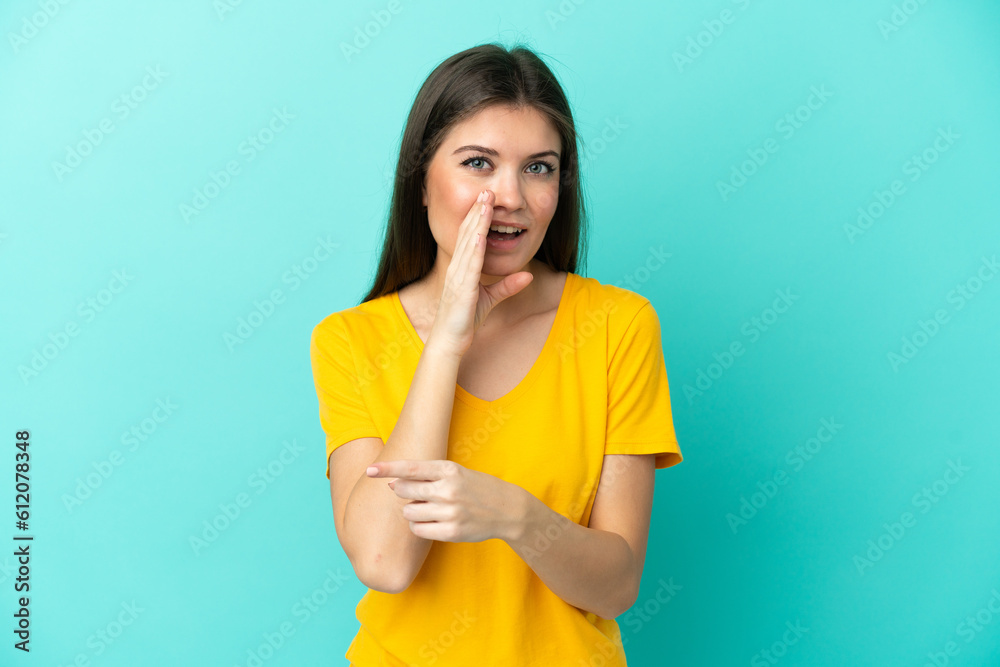 Young caucasian woman isolated on blue background pointing to the side to present a product and whispering something Young caucasian woman isolated on blue background pointing to the side to present a product and whispering something