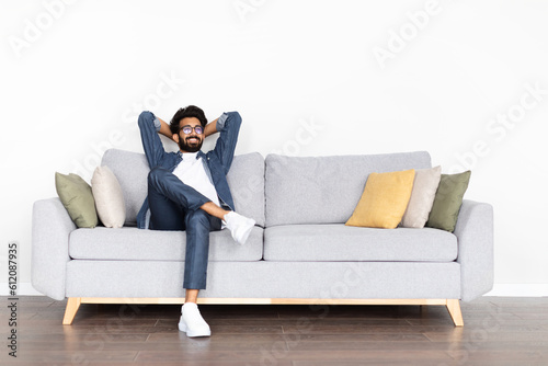 Foto Relaxed happy young eastern guy chilling on couch at home
