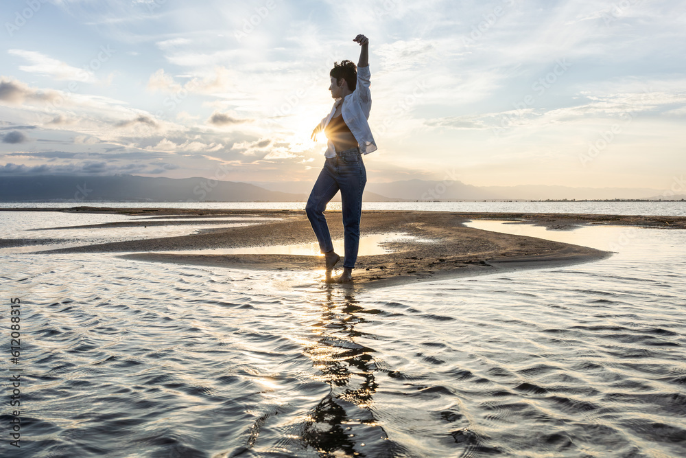 woman on the beach dancing at sunset in backlight with the sun behind in shadow, woman on vacation walking on the sand with golden water reflections from the sun at sunset, backlighting in the golden 