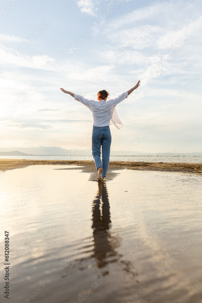 woman on the beach dancing at sunset in backlight with the sun behind in shadow, woman on vacation walking on the sand with golden water reflections from the sun at sunset, backlighting in the golden 