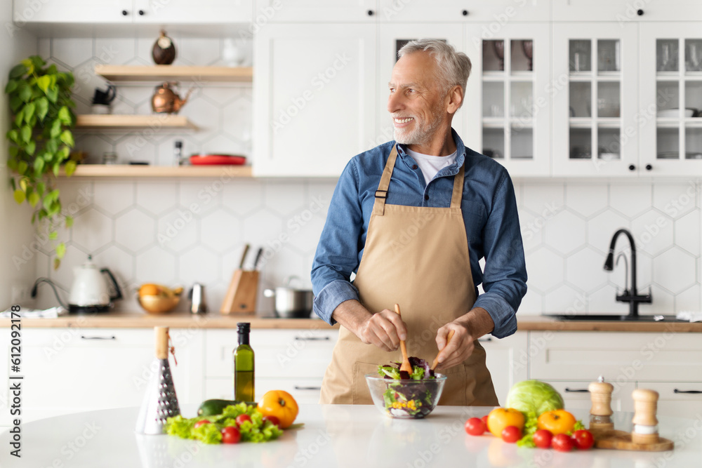 Happy Senior Man Cooking In Kitchen And Looking Aside At Copy Space