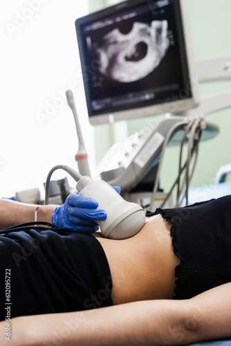 Close-up gynecologist conducts ultrasound scan for pregnant young woman on early pregnancy period and look on the screen in hospital. Pregnancy and maternity.