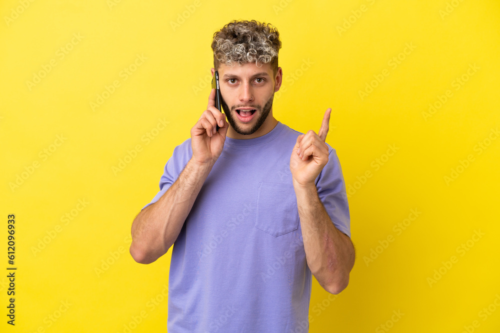 Young caucasian man using mobile phone isolated on yellow background intending to realizes the solution while lifting a finger up