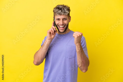 Young caucasian man using mobile phone isolated on yellow background celebrating a victory in winner position