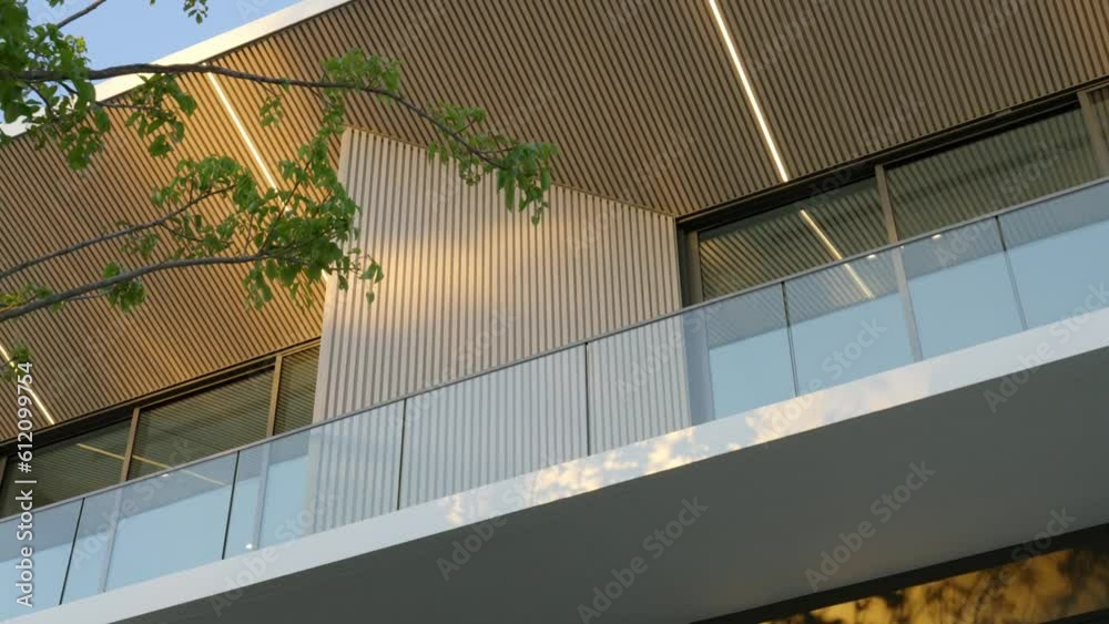 Low angle view of private two-storey villa with glass balcony and wooden panels. Exterior design of modern building among natural sunlight
