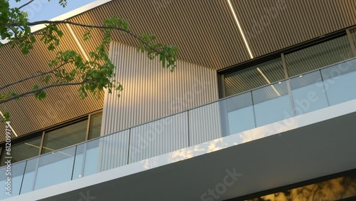 Low angle view of private two-storey villa with glass balcony and wooden panels. Exterior design of modern building among natural sunlight