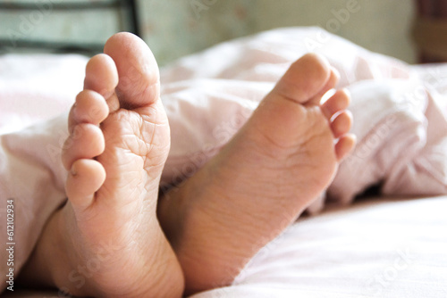 Feet under a light blanket on the bed. Concept of health