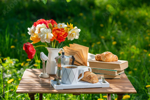 Bouquet of flowers, croissant, cup of tea or coffee, books on table in summer garden. Rest in garden, reading books, breakfast, vacations in nature concept. Summer time in garden on backyard