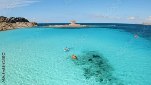 Aerial view of people on kayak and canoe in blue sea and old tower at summer sunny day. Clear azure water. La Pelosa beach, Sardinia island, Italy. Tropical. Sup boards. Active travel. Top drone view