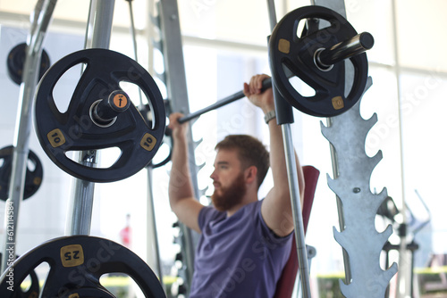 Young athletic man is training in the gym doing exercise with barbell