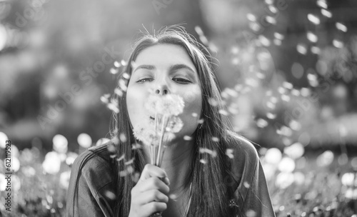 Beautiful Young Woman lying on the field in grass and blowing dandelions. Outdoors. Enjoy Nature. Healthy Smiling Girl on spring lawn. Allergy free concept. Freedom. Black and white shot