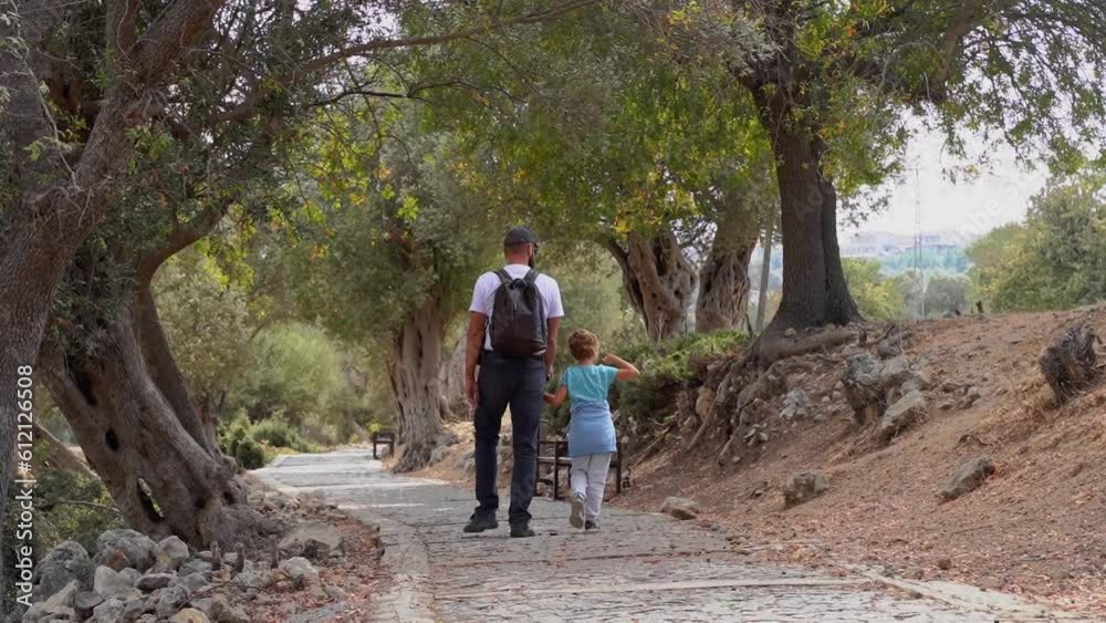 Travel with people. Caucasian father and his child boy or girl walking together path in ancient forest public park summer. Kid happily jumping. Family together leisure time activities.