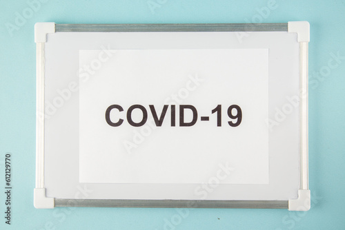 Above view of a sheet with covid- writing on white desk on blue background photo