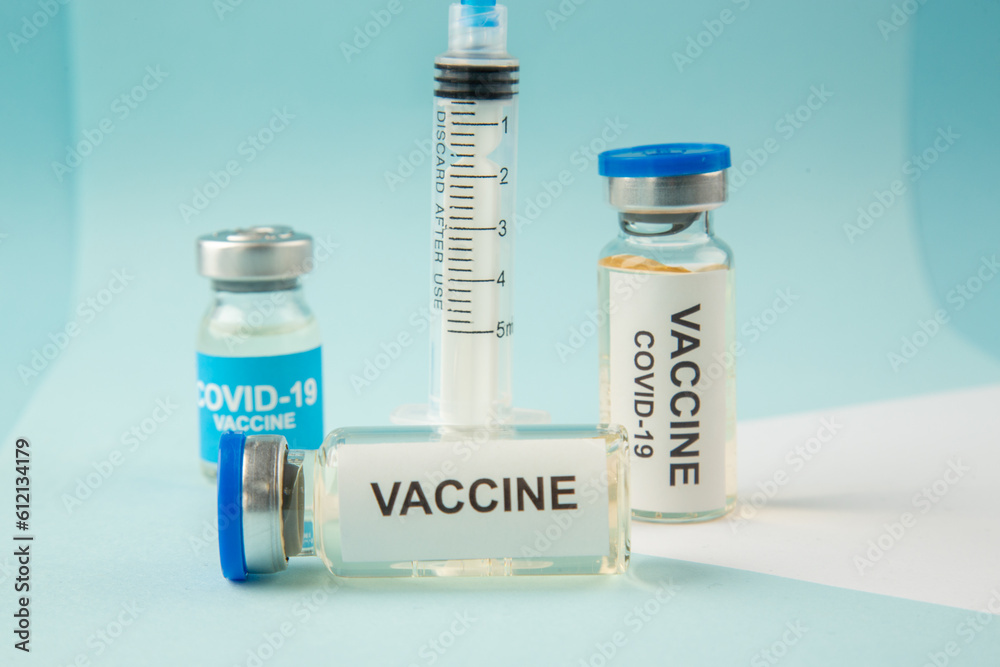 Close up view of covid- vaccine in medical ampoules and empty disposable syringe on a white blank on blue background Close up view of covid- vaccine in medical ampoules and empty disposable syringe on a white blank on blue background