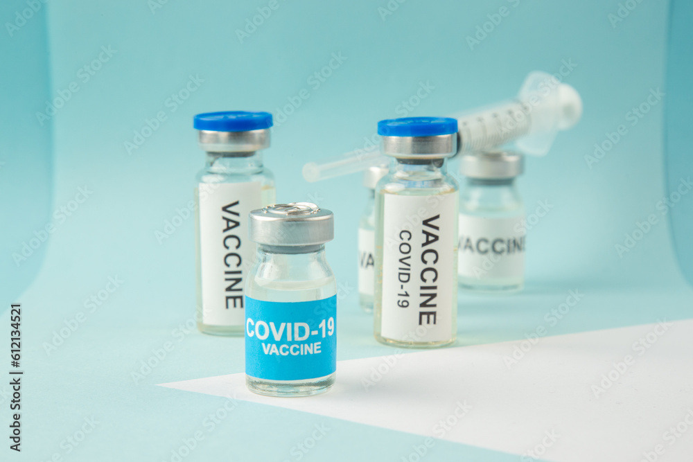 Close up view of COVID- vaccine ampoules and disposable syringe on pastel blue and white background Close up view of COVID- vaccine ampoules and disposable syringe on pastel blue and white background