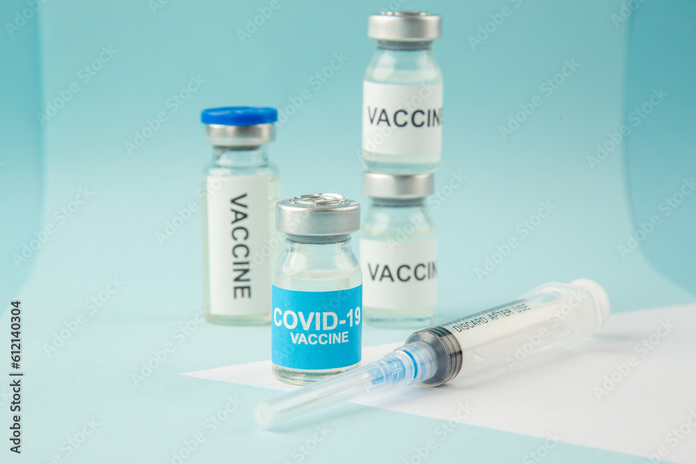 Front close view of COVID- vaccine ampoules and disposable syringe on pastel blue and white background Front close view of COVID- vaccine ampoules and disposable syringe on pastel blue and white background