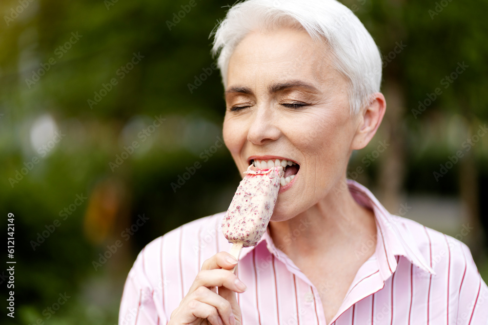 Portrait of happy stylish gray haired woman eating tasty ice cream with close eyes standing in park. Summer vacation, positive lifestyle concept Portrait of happy stylish gray haired woman eating tasty ice cream with close eyes standing in park. Summer vacation, positive lifestyle concept