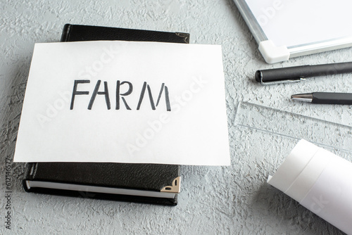 Front view of FARM writing on white sheet on black notebook pens ruler desk blank on gray sand background photo