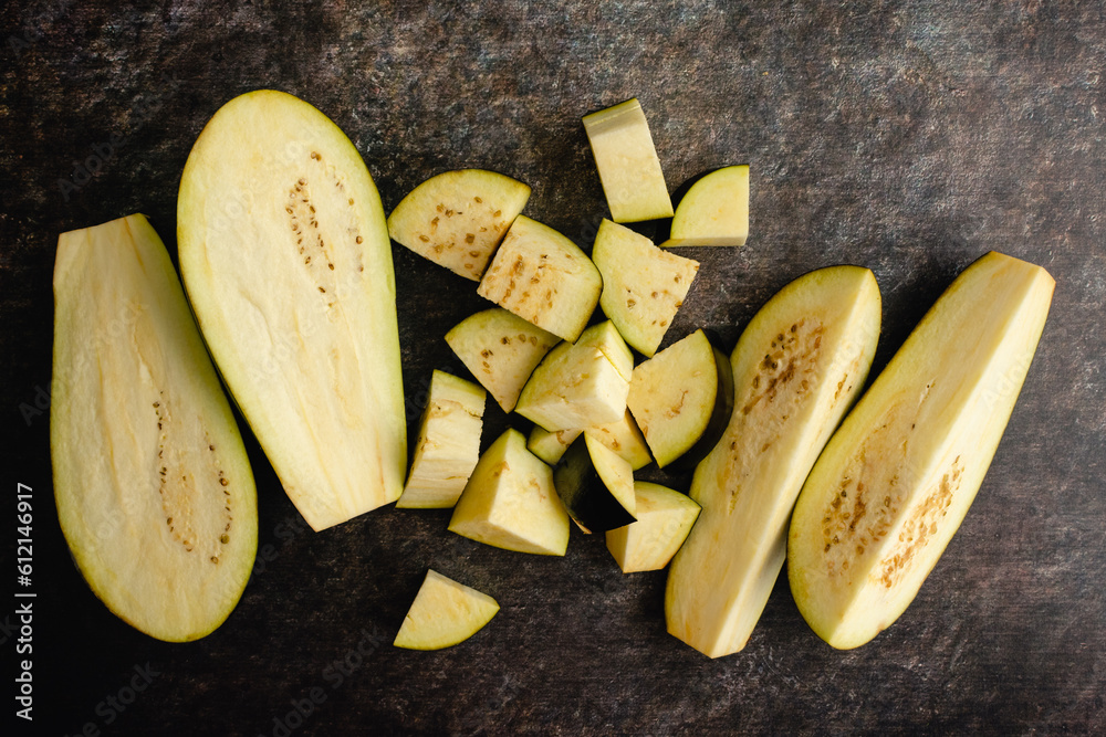 Eggplant Chopped into Halves, Quarters, and Large Pieces: Two raw unpeeled aubergines cut into a variety of sizes on a dark background