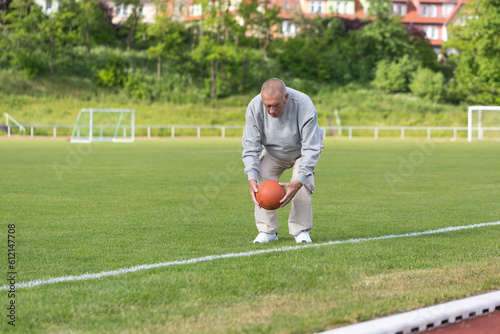 An elderly man goes in for sports on the background of the stadium on a summer evening
