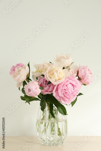 Bouquet of beautiful peonies in glass vase on beige table