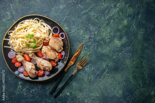 Overhead view of raw pastas chickens and vegetables on a plate and cutlery set on the right side on green black mix colors background