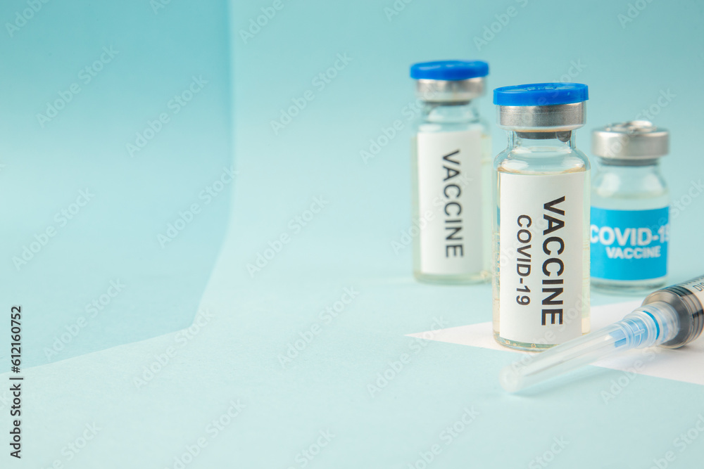 Side view of COVID- vaccine ampoules and disposable syringe on the left side on pastel blue and white background