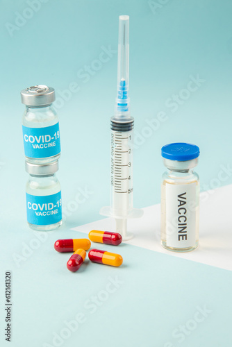 Side view of empty disposable syringe and capsules on a white blank covid- vaccines on blue background