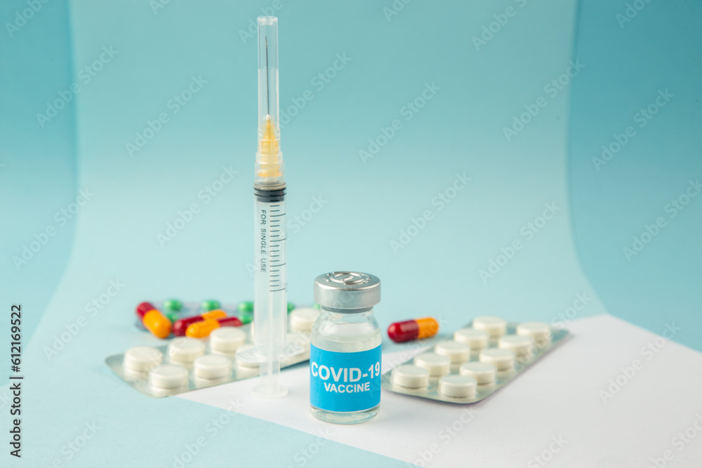 Top view of COVID- vaccine in medical ampoules on white sheet packed pills and capsules syringe on blue wave background Top view of COVID- vaccine in medical ampoules on white sheet packed pills and capsules syringe on blue wave background