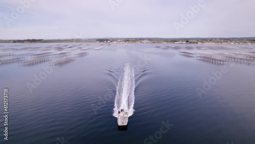 Aerial drone shot of a motorboat sailing in a shellfish farm during sunset in Sete, France.