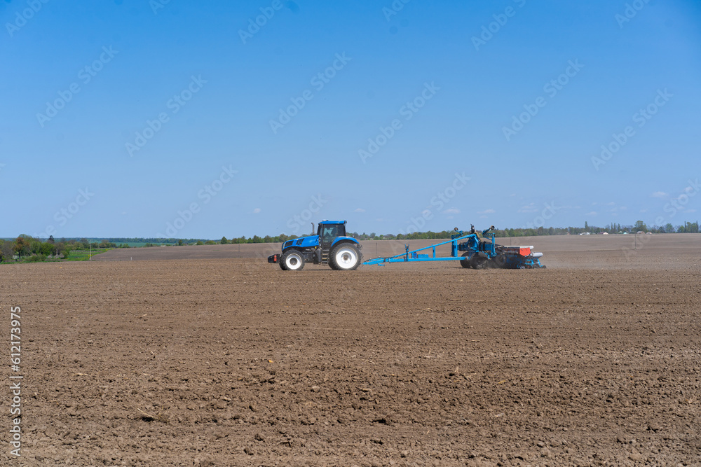 Obraz premium The tractor drives across the field and cultivates the land. Agricultural vehicle works in countryside. Sowing is the process of planting seeds in the ground as part of the early spring time
