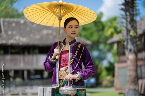 Beautiful pretty young Asian woman wearing a millionaire traditional Thai dress Lanna style standing with an antique silver bag and umbrella in a green natural park.