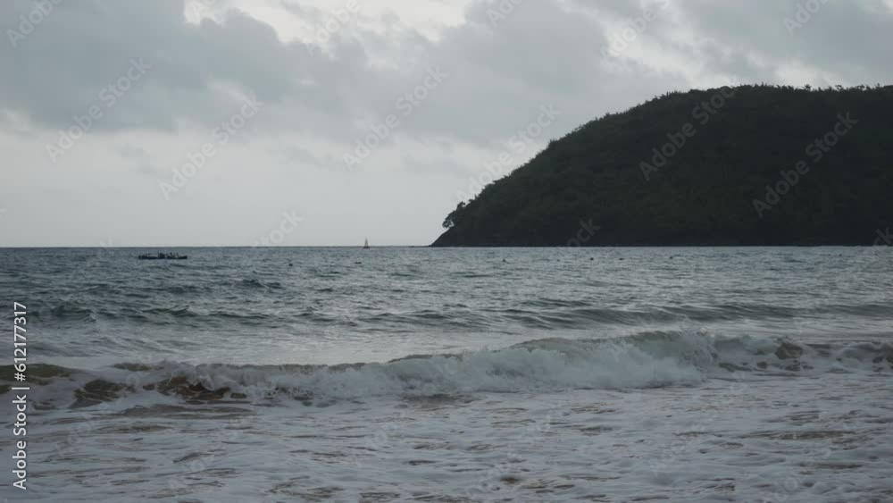 Dark morning shot of ocean waves crashing onto the sandy beach of Con Dao Island in Vietnam. In the background, a dark mountain, the sky, and clouds are visible. Dark morning shot of ocean waves crashing onto the sandy beach of Con Dao Island in Vietnam. In the background, a dark mountain, the sky, and clouds are visible.