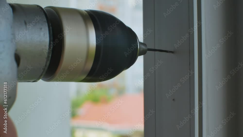 Worker drills holes in plastic window frame with electric drill. An